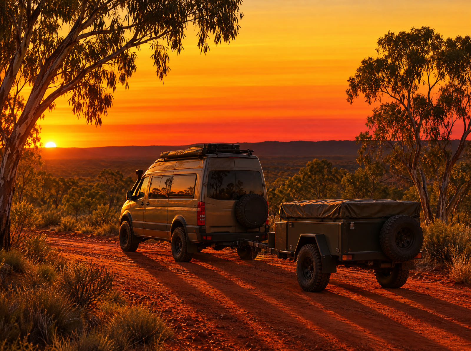 A touring van and trailer on a red dirt road at sunrise